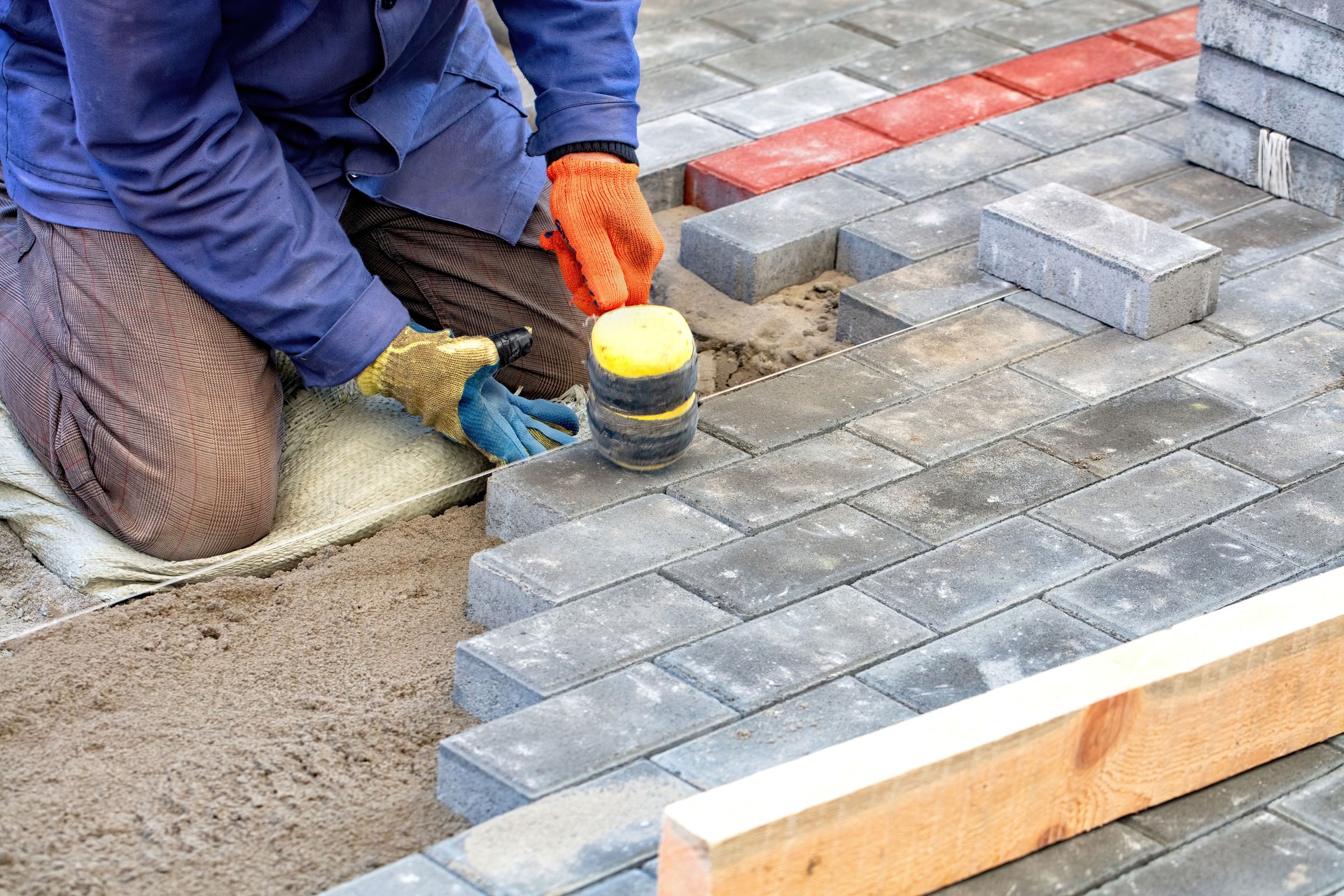 Craftsman diligently laying paving stones in a vibrant outdoor project during bright daylight. Copy space.